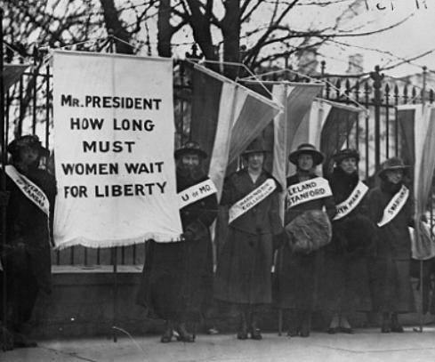 Study the image. Early 1900s women wearing sashes hold a banner that states  What is being supported