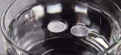 A coin floats on the top of a glass of water.

Explain why the coin is able to float on top of the